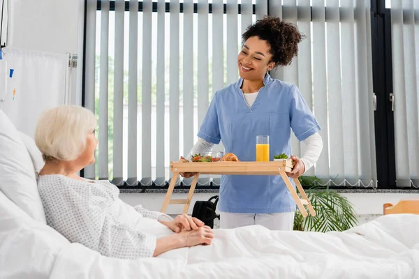 Усміхнена Афроамериканська Медсестра Тримає Сніданок Апельсиновий Сік Підносі Біля Пацієнта — стокове фото