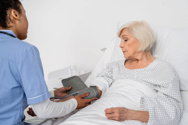 African american nurse fastening tonometer on hand of senior patient 