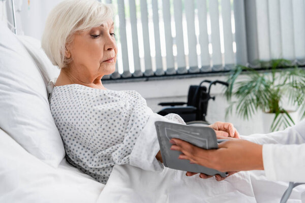 Senior woman looking at african american nurse with tonometer on blurred foreground in clinic 