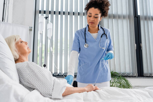 African american nurse holding catheter near elderly patient in clinic 