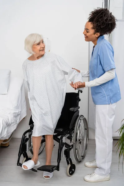 Enfermera Afroamericana Sonriente Cogida Mano Del Paciente Cerca Silla Ruedas — Foto de Stock