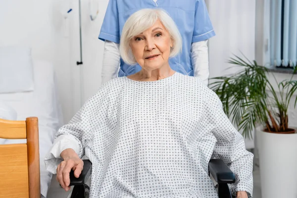 Senior Kvinna Rullstol Tittar Kameran Nära Sjuksköterska Kliniken — Stockfoto