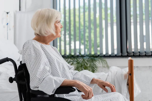 Side view of woman sitting in wheelchair near hospital bed