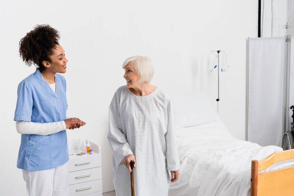 Patient with walking cane looking at smiling african american nurse 