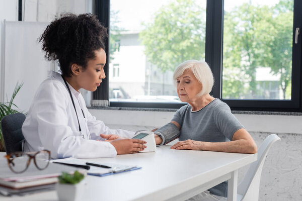 African american doctor checking pressure of senior woman with tonometer 