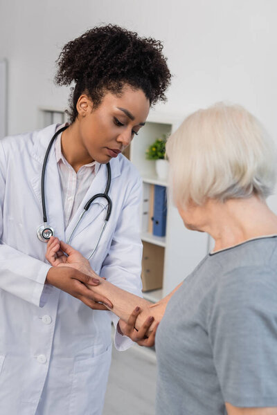 African american traumatologist checking injured arm of senior patient 