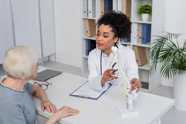 Médico Afro Americano Olhando Para Mulher Idosa Perto Modelo Coluna — Fotografia de Stock