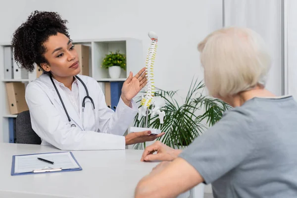 Blurred Patient Sitting African American Doctor Holding Spine Model — Stock Photo, Image
