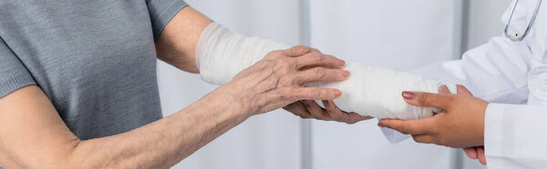 Cropped view of african american doctor touching arm of patient in plaster bandage, banner 
