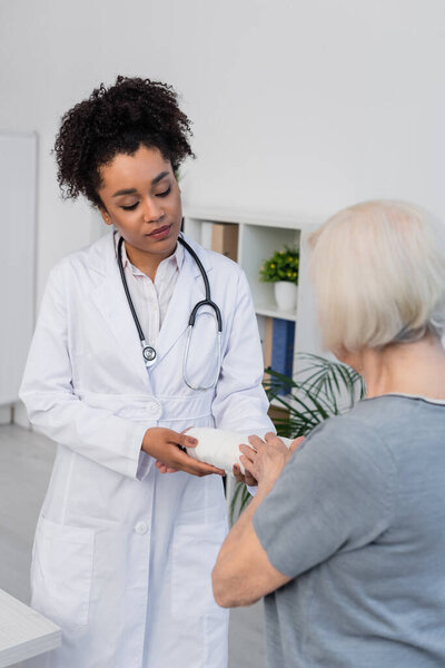 African american traumatologist holding arm of senior woman in plaster bandage 