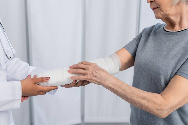 Cropped view of senior woman with plaster bandage on arm standing near african american doctor 