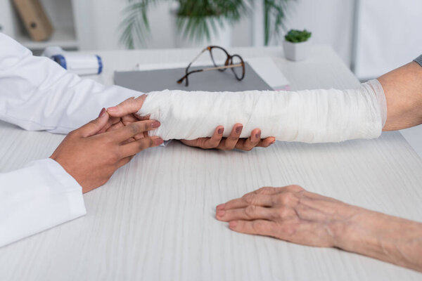 Cropped view of african american doctor touching and checking broken arm of patient 