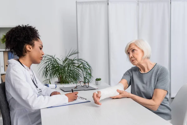 Femme Âgée Avec Bandage Plâtre Sur Bras Regardant Médecin Afro — Photo