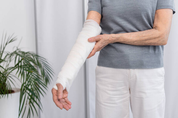 Обрезанный вид пожилой женщины, касающейся руки в гипсовой повязке в клинике 