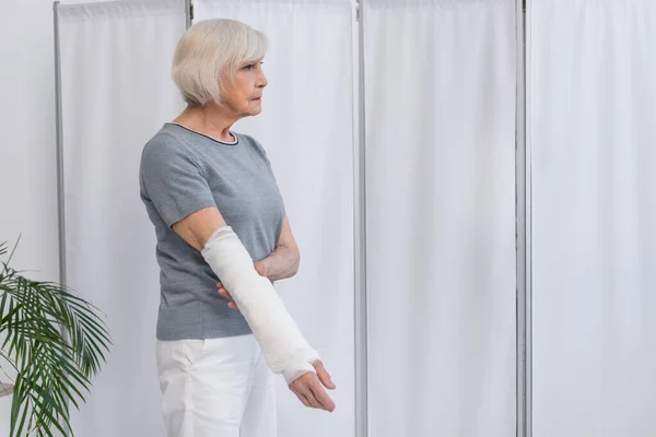 站立在诊所的老年患者骨折手臂上石膏绷带侧视图 — 图库照片