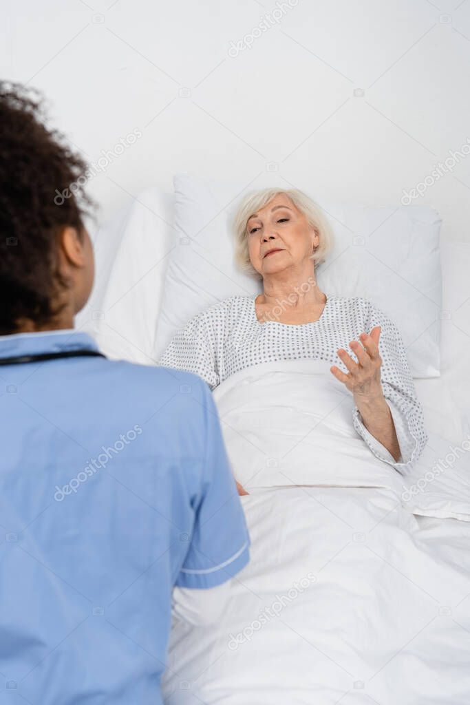 Senior patient talking to african american nurse in hospital ward 