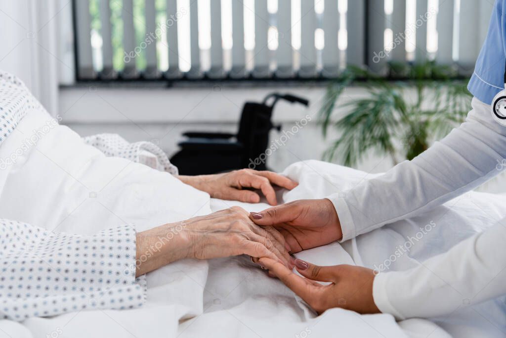 Cropped view of african american nurse holding hand of elderly patient 