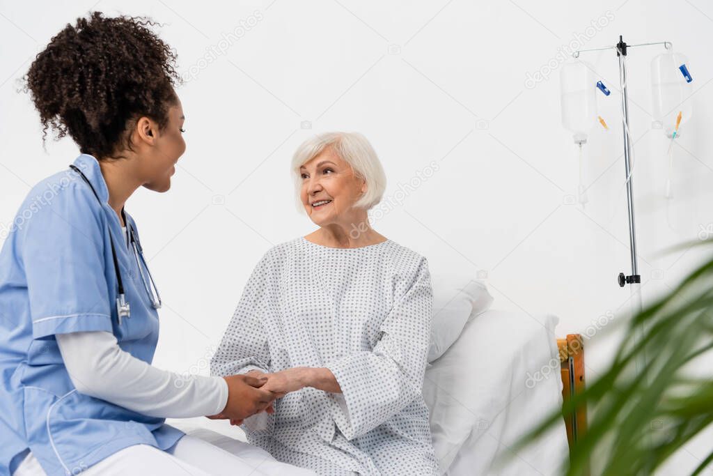 African american nurse talking to smiling senior patient on hospital bed 