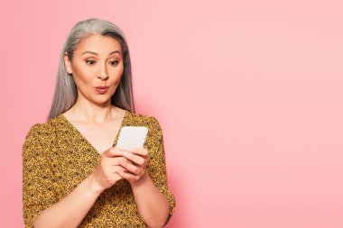 Şaşırmış Asyalı kadın bluzuyla cep telefonundan pembe bir mesaj yolluyor.