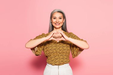 Sarı bluzlu memnun Asyalı kadın. Pembe arka planda kalp sembolü var.