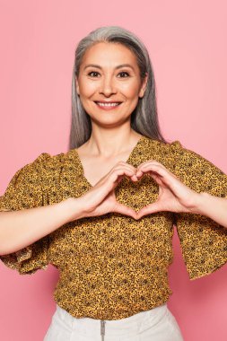 Gri saçlı mutlu Asyalı kadın, pembe ellerle kalp işareti gösteriyor.