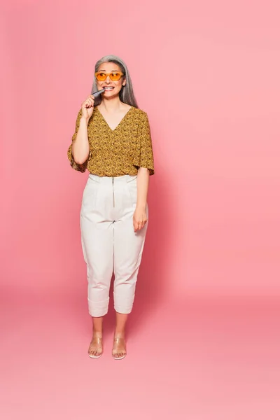 Pembe Arka Planda Kredi Kartını Isıran Modaya Uygun Giyinmiş Asyalı — Stok fotoğraf