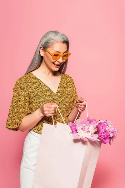 Amazed Asian Woman Looking Shopping Bag Peonies Isolated Pink — Stock Photo, Image