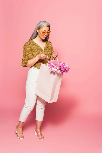 穿着白色裤子的亚洲女人惊讶地看着粉色衬托的购物袋 — 图库照片