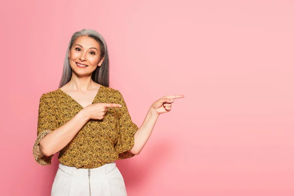 Positieve Aziatische Vrouw Wijzend Met Vingers Terwijl Glimlachen Camera Roze — Stockfoto