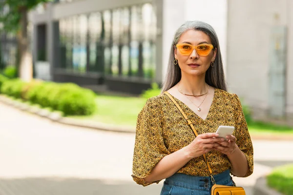 Grey Haired Asian Woman Patterned Blouse Yellow Sunglasses Standing Smartphone — Stock Photo, Image
