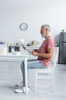 Mutfakta süt ve mısır gevreğinin yanında gazete okuyan adamın yan görüntüsü 