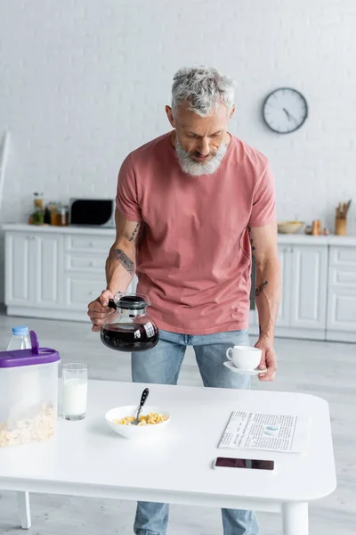 Volwassen Man Met Koffiepot Kopje Buurt Van Ontbijt Krant Smartphone — Stockfoto