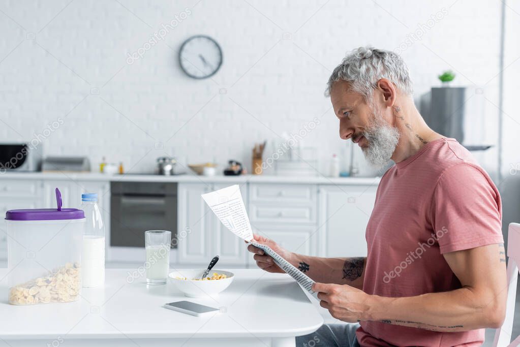 Side view of mature man reading news near smartphone and breakfast 