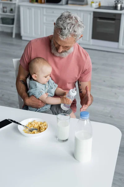 Man Houdt Baby Dochter Met Fles Buurt Van Het Ontbijt — Stockfoto