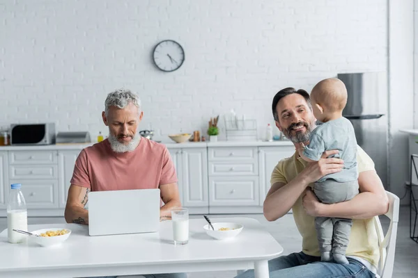 Uomo Omosessuale Sorridente Che Tiene Bambina Vicino Partner Usando Laptop — Foto Stock