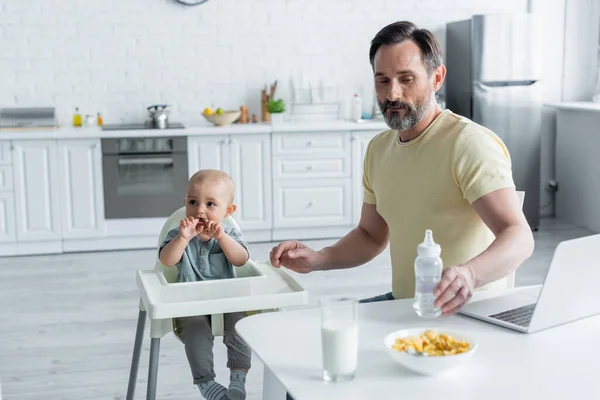 Mature Man Holding Baby Bottle Laptop Breakfast Daughter High Chair — Stock Photo, Image