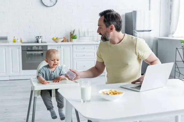 Father Holding Baby Bottle Crying Daughter Laptop Kitchen — Stock Photo, Image