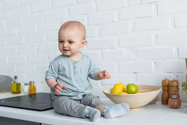 坐在厨房工作台上水果旁边微笑的婴儿 — 图库照片