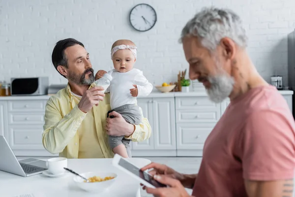 Homosexual Man Bottle Milk Holding Baby Daughter Partner Laptop Kitchen — Stock Photo, Image