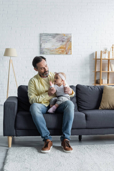 Mature man holding toddler kid on couch 