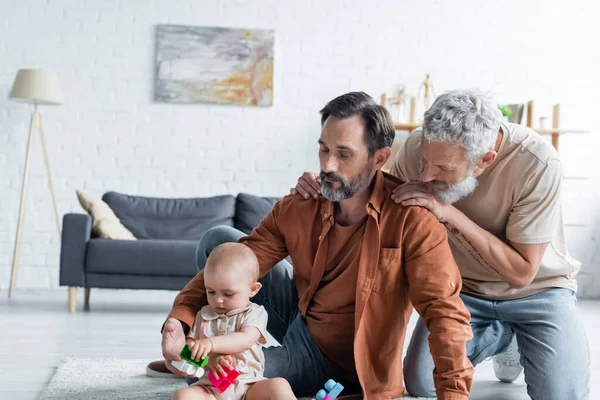 Homosexueller Mann Umarmt Lebensgefährtin Nahe Tochter Mit Bauklötzen Auf Teppich — Stockfoto