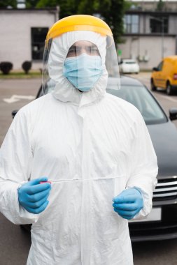 PCR testi yapan koruyucu vizörlü bir tıp çalışanı açık havada bulanık arabanın yanında. 