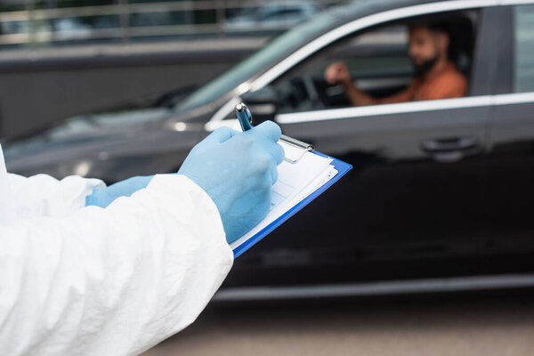 Medical worker writing on clipboard near blurred driver in car 