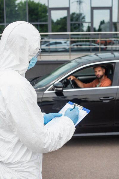 Medical worker writing on clipboard near driver in car on blurred background 