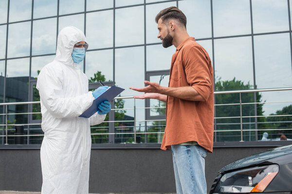 Man talking to border guard in hazmat suit writing on clipboard near car 