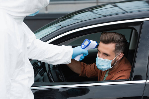 Border guard in hazmat suit checking temperature of driver in auto 