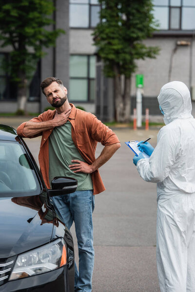Sick driver standing near car and medical worker writing on clipboard 