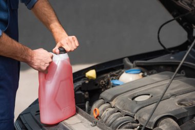 Cropped view of mechanic holding windshield washer fluid near car  clipart