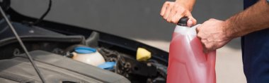 Cropped view of mechanic opening windshield washer fluid near blurred car, banner  clipart