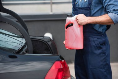 Cropped view of repairman holding canister of windshield washer fluid near auto  clipart